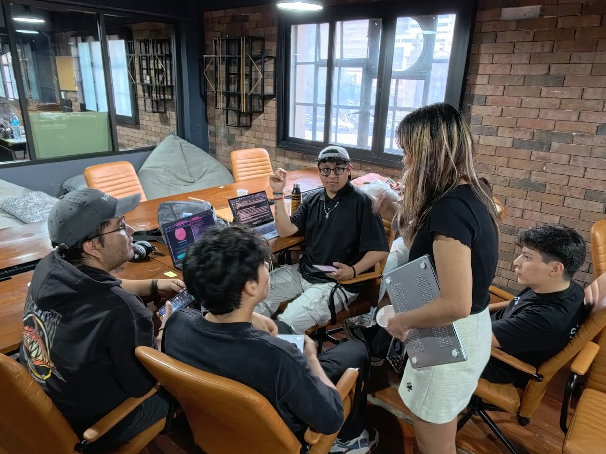 Mafer Galindo de pie con una laptop frente a un equipo en un hackathon
